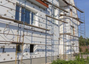 The process of building wall insulation using polystyrene in the open air. Scaffold on house, renovation. House for renovation with the scaffolding for workers on building, close up
